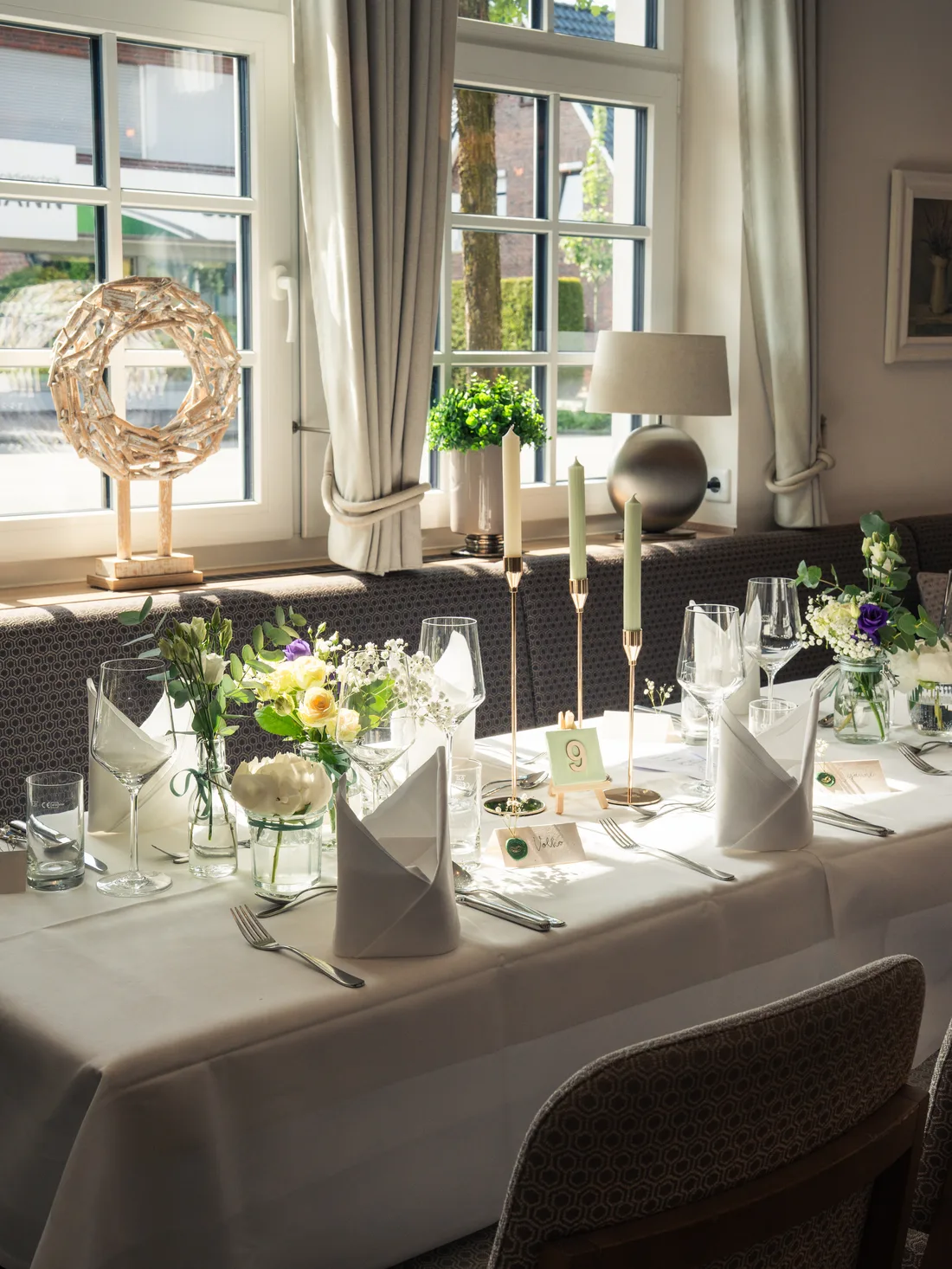 Hochzeitstafel mit Blumen, Kerzen und Tischkarten im Fensterlicht